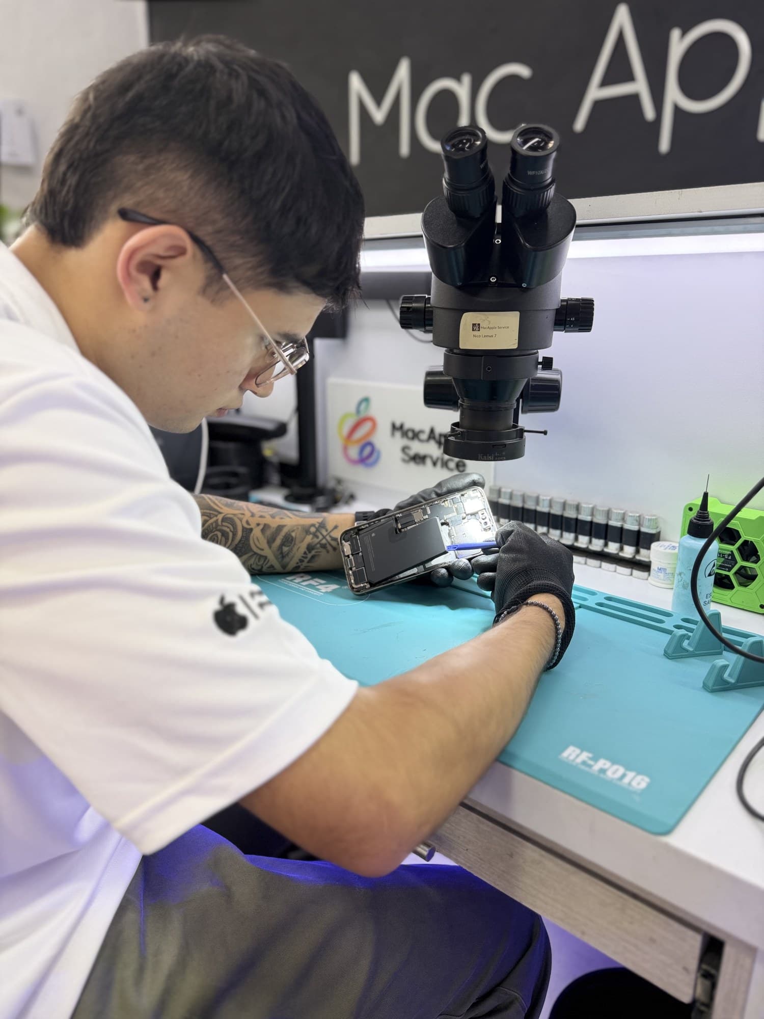 Técnico reparando placa lógica de iPhone con microscopio binocular profesional en MacApple Service Fusagasugá